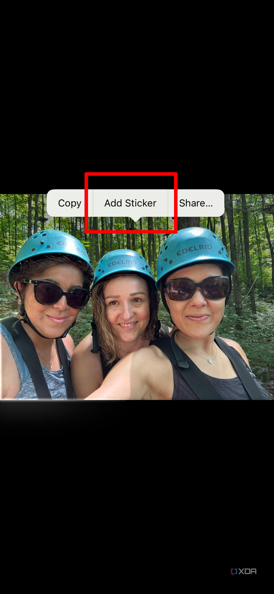 A photo from an iPhone library showing three women smiling wearing headgear, the add sticker pop-up selected.