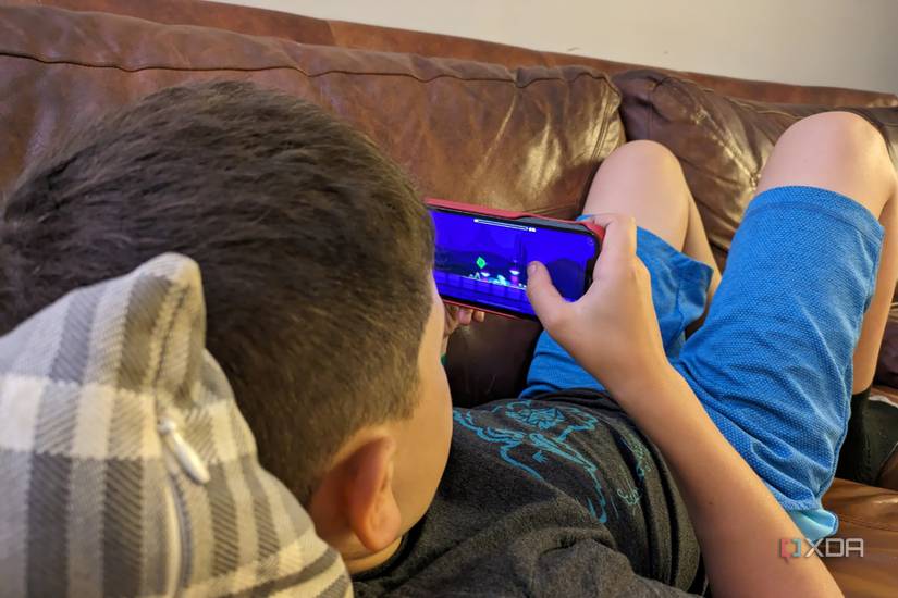 A young boy lying on a couch playing on an iPhone.