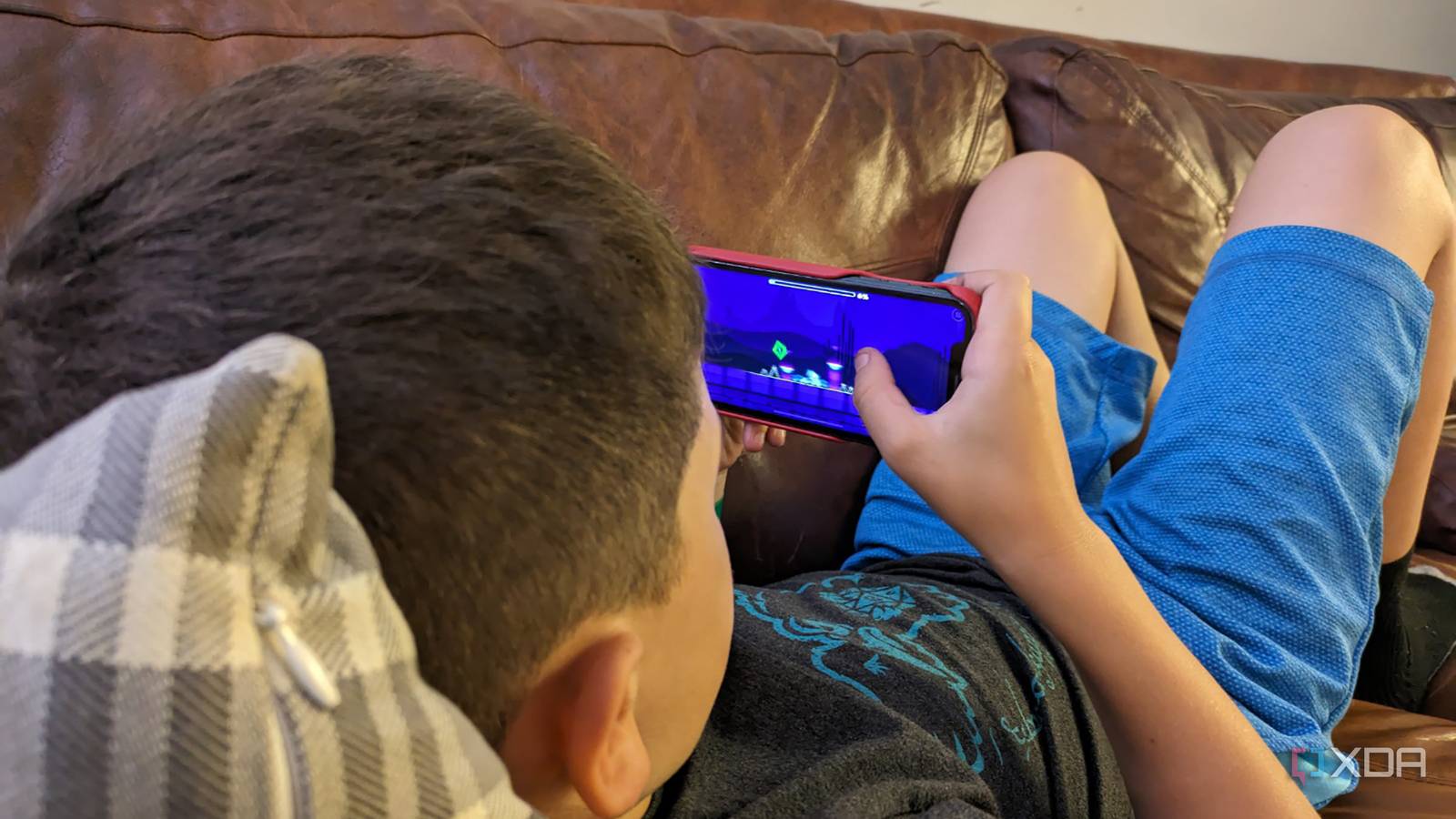 A young boy lying on a couch playing on an iPhone.