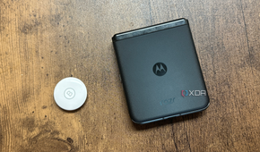 An Apple AirTag next to a Motorola Razr+ against a wood background.