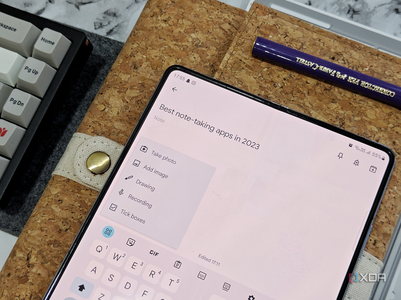 An image showing a Galaxy Z Fold 5 displaying the Google Keep app over a physical notepad next to a keyboard.