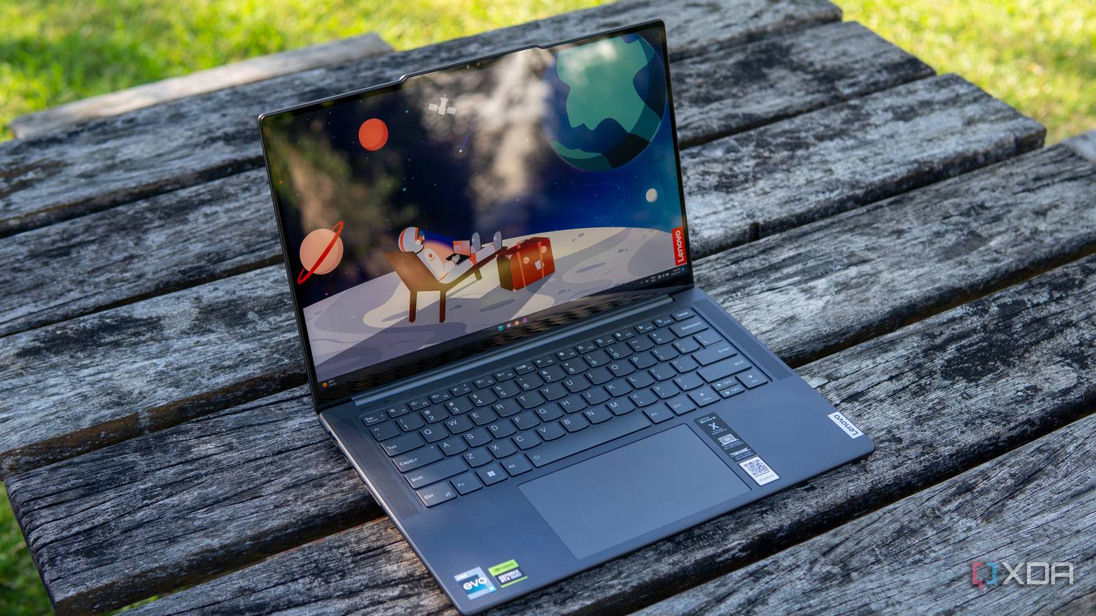 Angled view of a Lenovo Slim Pro 9i 14-inch laptop on a wooden table with grass in the background