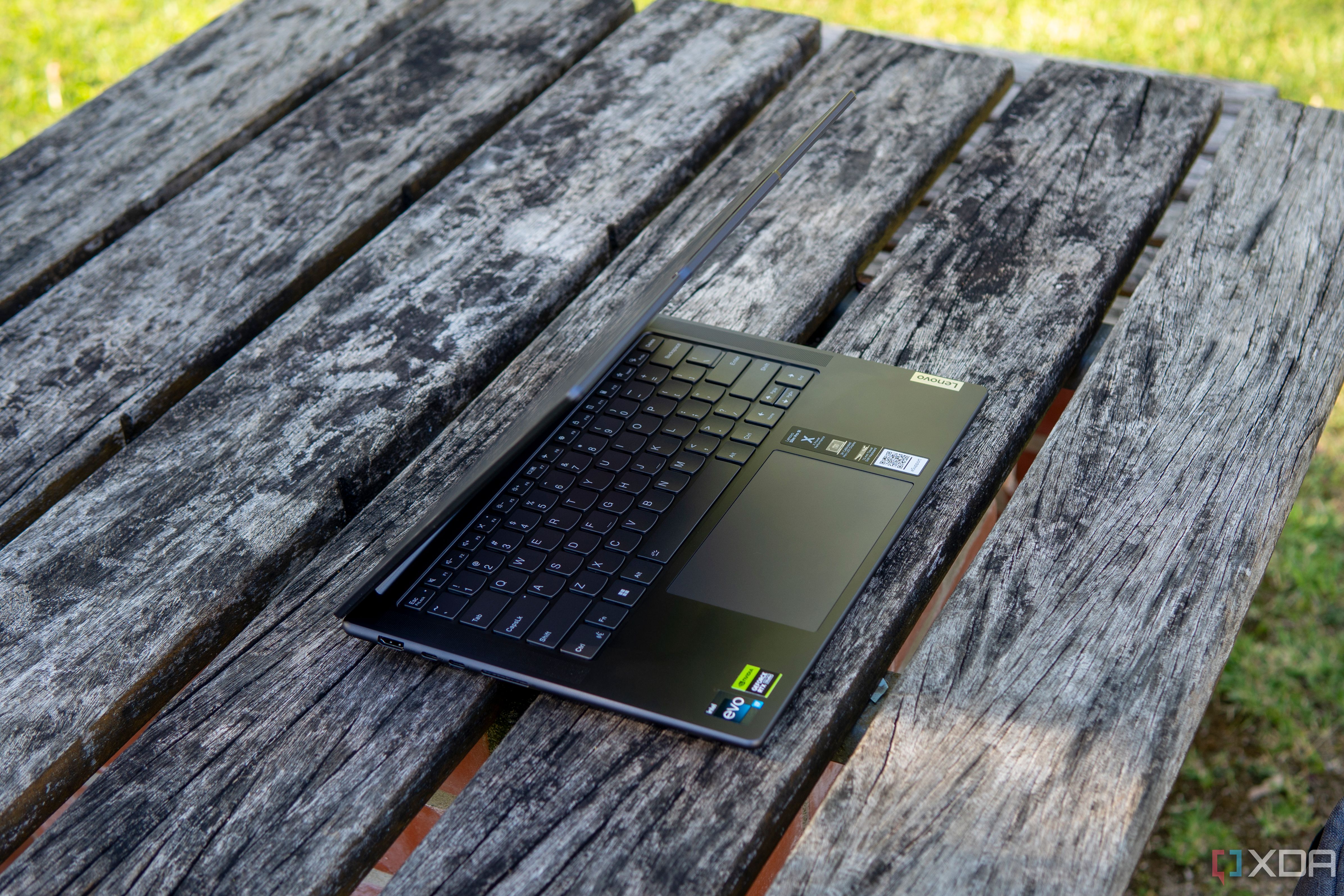 Angled view of the Lenovo Slim Pro 9i 14-inch model on a wooden table with the lid open at roughly 60 degrees