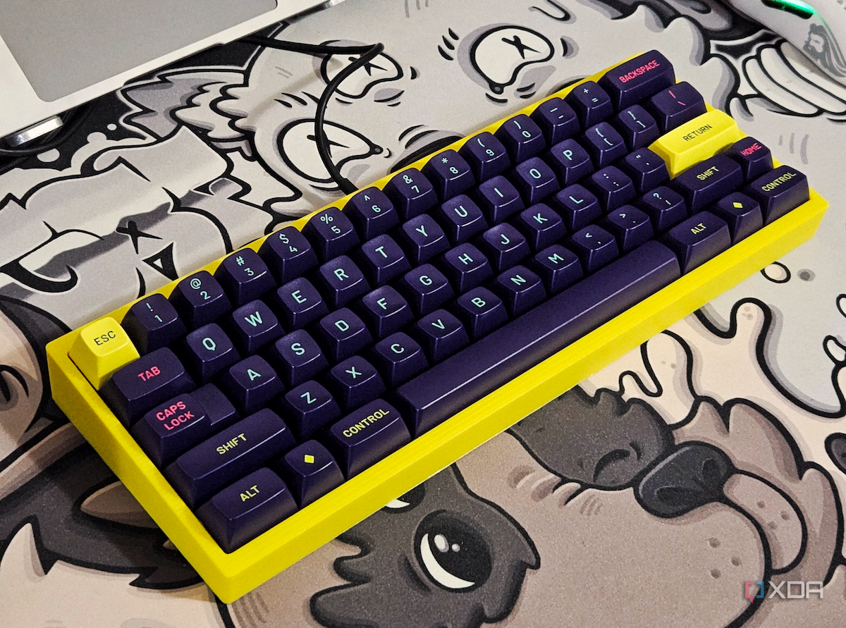 A render showing a mechanical keyboard with a yellow case and purple keycaps on a GAF deskmat.