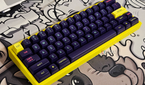 A render showing a mechanical keyboard with a yellow case and purple keycaps on a GAF deskmat.