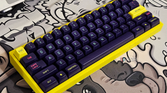 A render showing a mechanical keyboard with a yellow case and purple keycaps on a GAF deskmat.