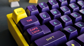 An image of a mechanical keyboard with a yellow case and purple MT3 keycaps.