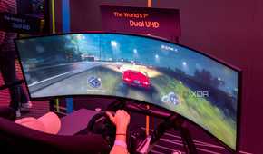 A Samsung Odyssey Neo G9 57-inch monitor displaying a racing game being played with a steering wheel.