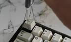 An image showing a keycap puller removing the escape key from a mechanical keyboard.