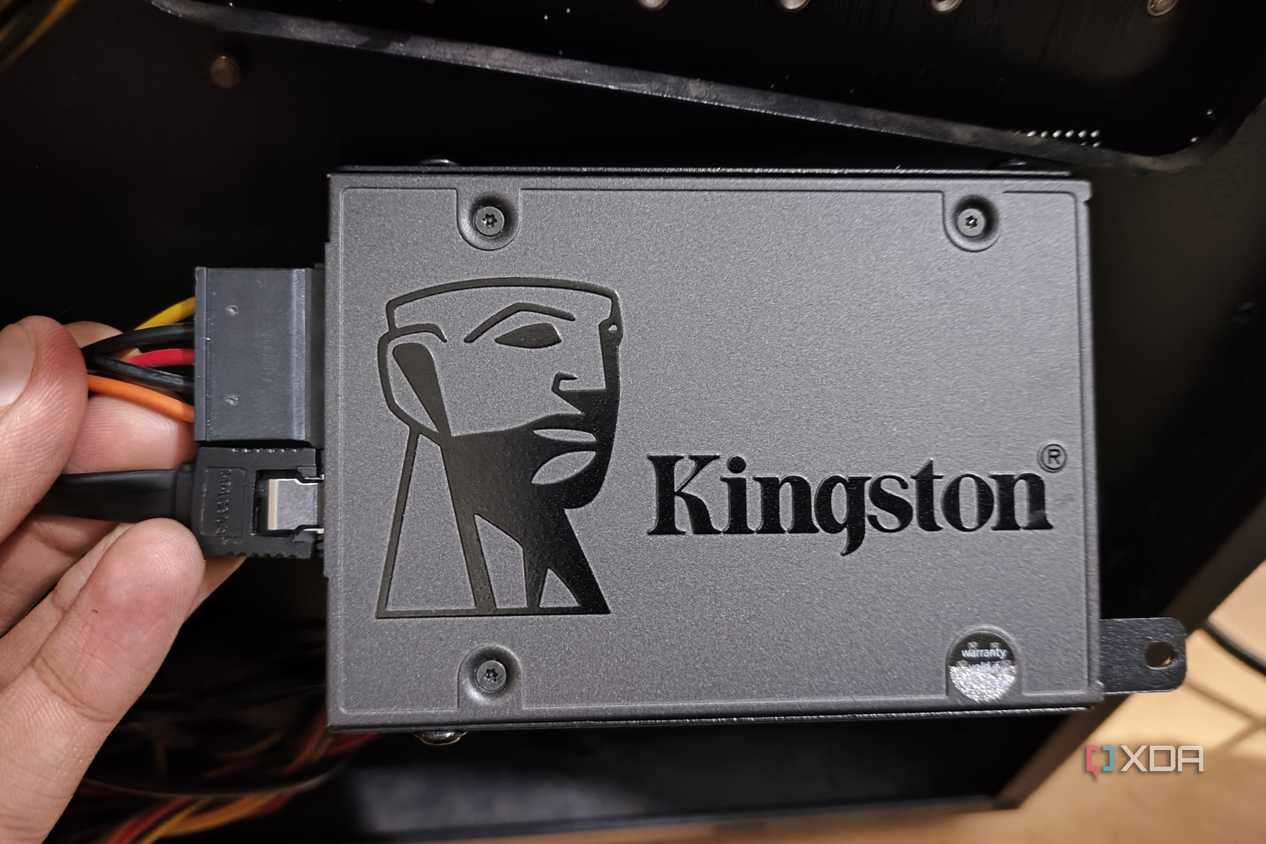 A person holding an SSD with the SATA data and power cables plugged in