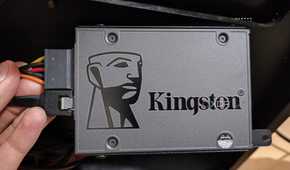 A person holding an SSD with the SATA data and power cables plugged in