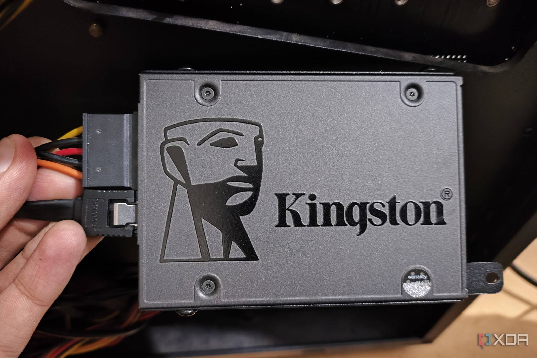 A person holding an SSD with the SATA data and power cables plugged in