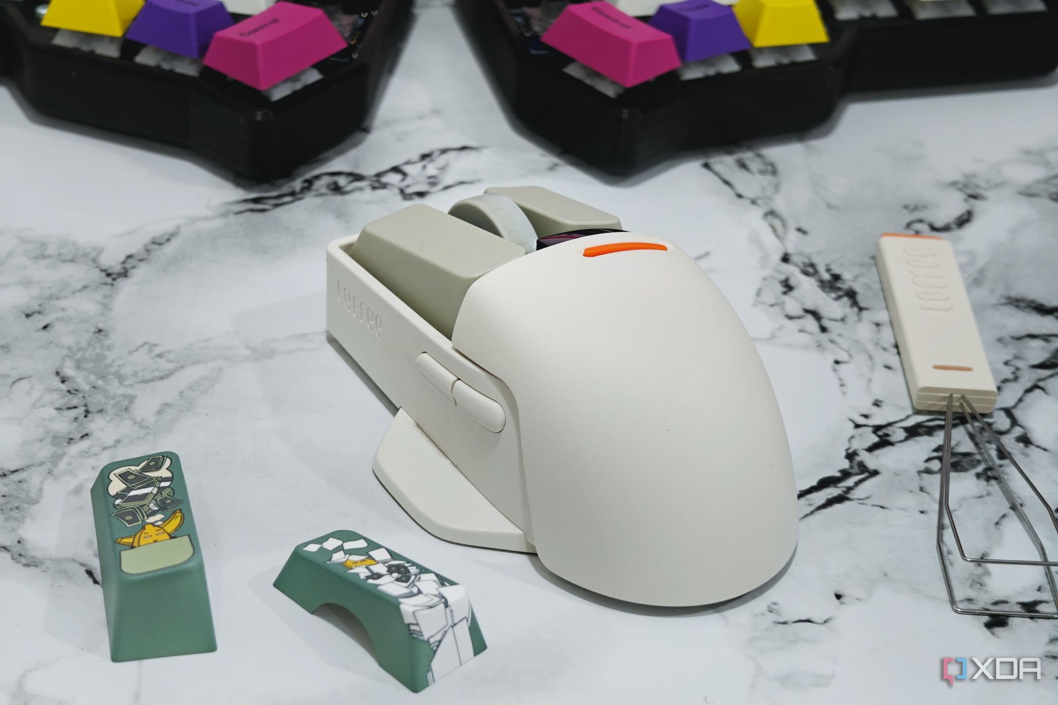 An image showing a Lofree PBT wireless mouse sitting on a desk next to some keycaps and a keycap puller.