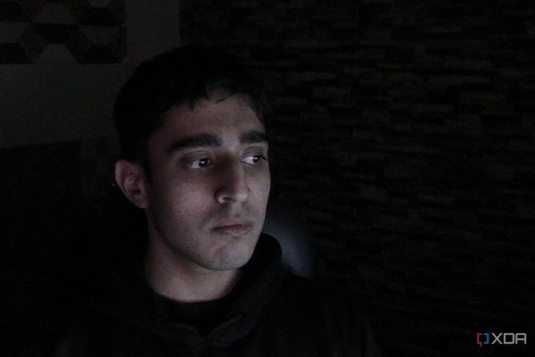 An image of a man sitting far away from the OBSBOT Tail Air webcam in a dark room