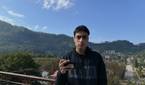 A man holding a Poco F5, with a panoramic sight behind him