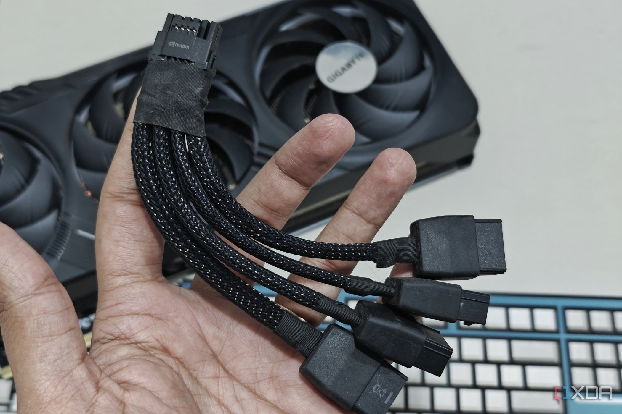 An image showing a person holding a 12VHPWR adapter cable in hand with the Gigabyte GeForce RTX 4070 Ti Gaming OC GPU in the background.