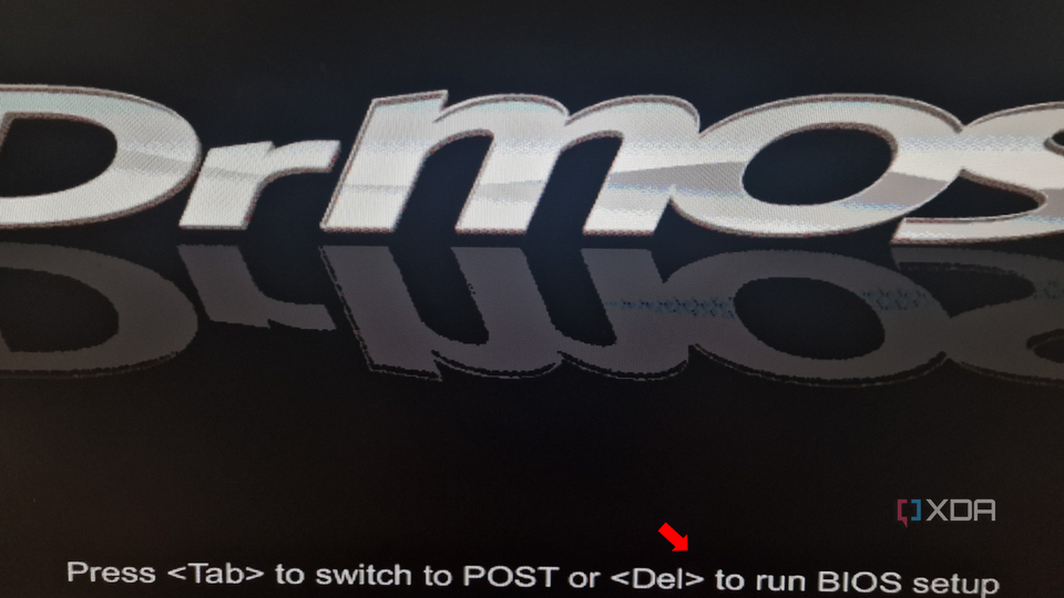 A close-up of a computer screen displaying BIOS boot text "Press <Tab> to switch to POST or <Del> to run BIOS setup" with the BIOS version name partially visible at the top and a red arrow pointing to an option.