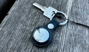 Apple AirTag keychain with a key placed on a wooden bench