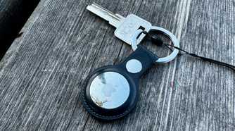 Apple AirTag keychain with a key placed on a wooden bench