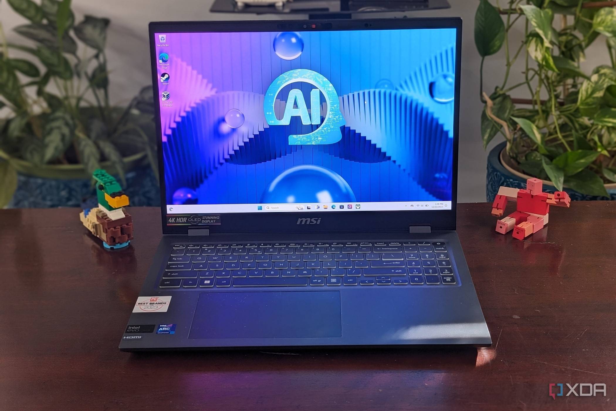 A photo of the MSI Prestige Evo 16 AI sitting on a desk with plants and toy objects in the background