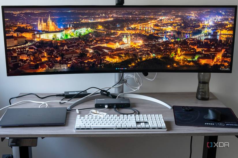A desk setup with a monitor, keyboard, mouse, webcam, and a laptop, all of which are connected to the Plugable TBT4-UDX1 docking station
