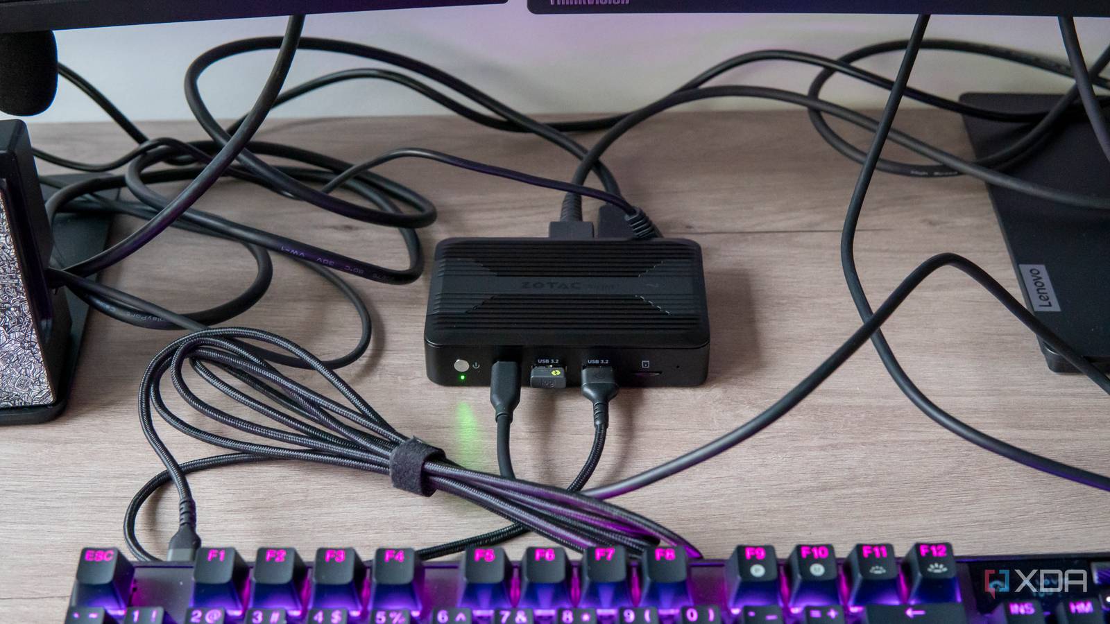 A Aotac Zbox Pico PI430AJ with multiple peripherals connected to it on a desk. A keyboard and two monitors are visible in the corners of the frame