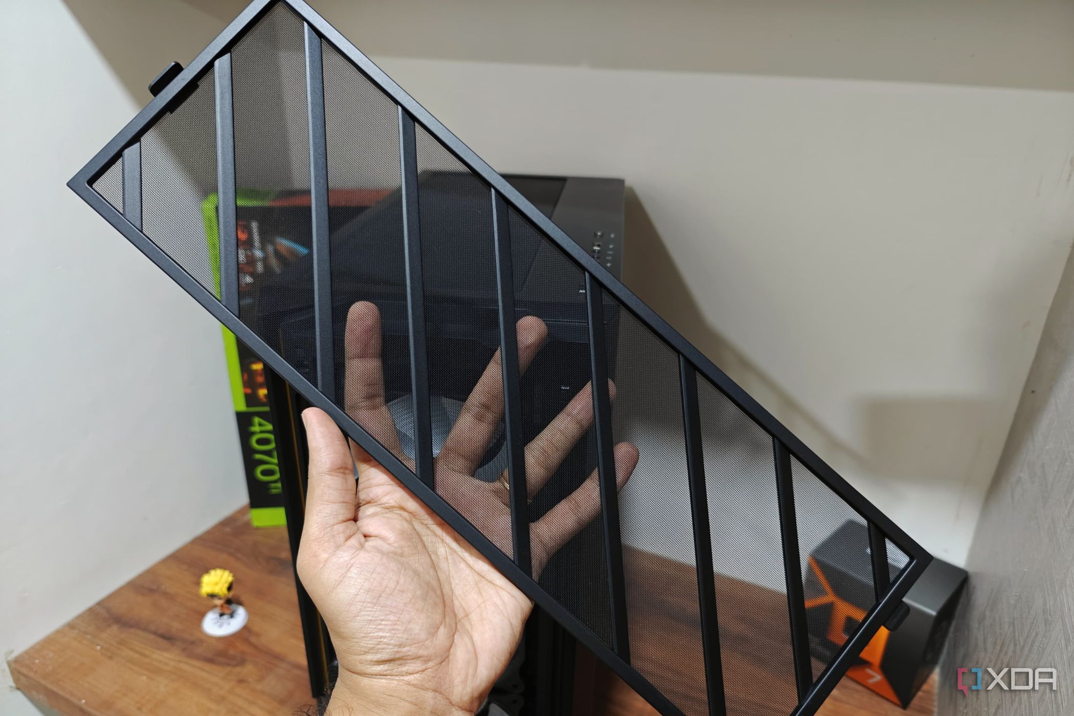 An image showing a person holding the front mesh panel with a PC case and a desk in the background.