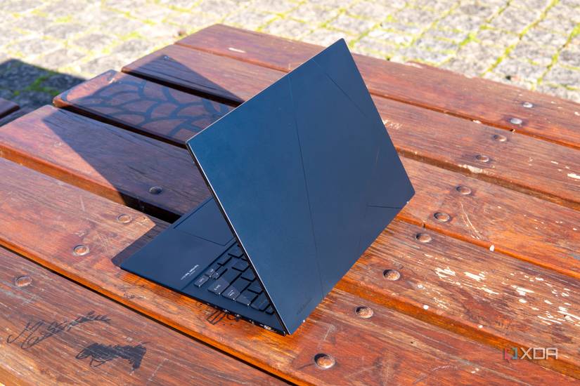 Angled rear view of the Asus Zenbook 14 OLED with the lid open at 60 degrees on an outdoor wooden table