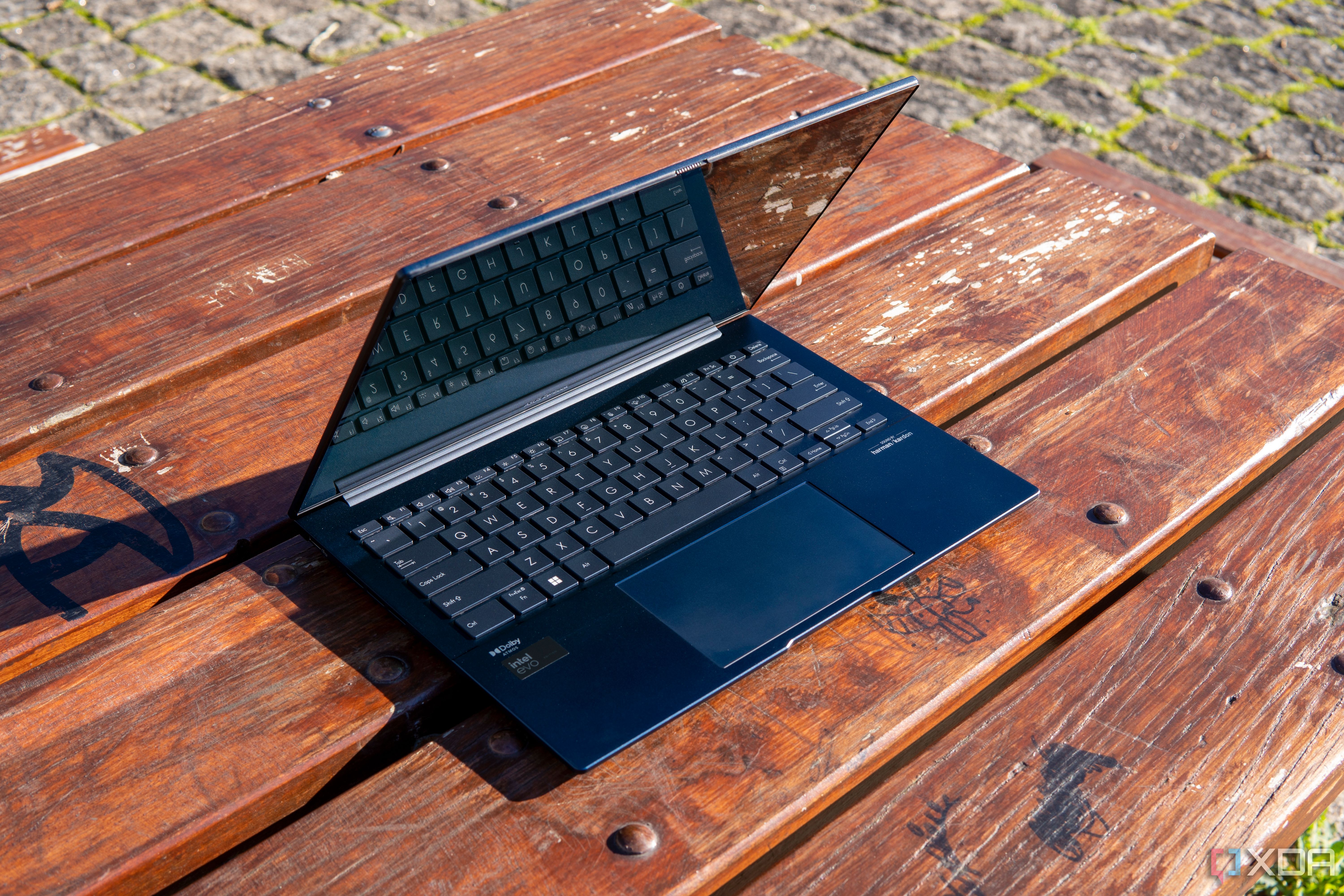 Angled front view of the Asus Zenbook 14 OLED with the lid open at about 70 degrees on a wooden outdoor table