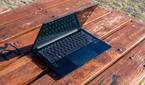 Angled front view of the Asus Zenbook 14 OLED with the lid open at about 70 degrees on a wooden outdoor table