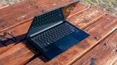Angled front view of the Asus Zenbook 14 OLED with the lid open at about 70 degrees on a wooden outdoor table