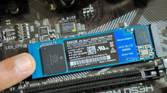 An image showing a person holding an M.2 SSD module in place with their finger.