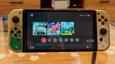 Front view of the Nintendo Switch OLED model displaying the Home menu with a game running in the background