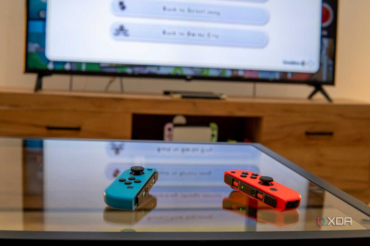 A pair of Joy-Con controllers on a table with a Nintendo Switch connected to a TV in the background