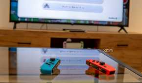 A pair of Joy-Con controllers on a table with a Nintendo Switch connected to a TV in the background