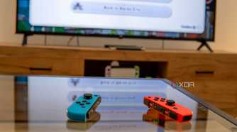 A pair of Joy-Con controllers on a table with a Nintendo Switch connected to a TV in the background