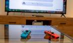A pair of Joy-Con controllers on a table with a Nintendo Switch connected to a TV in the background