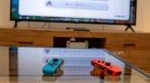 A pair of Joy-Con controllers on a table with a Nintendo Switch connected to a TV in the background