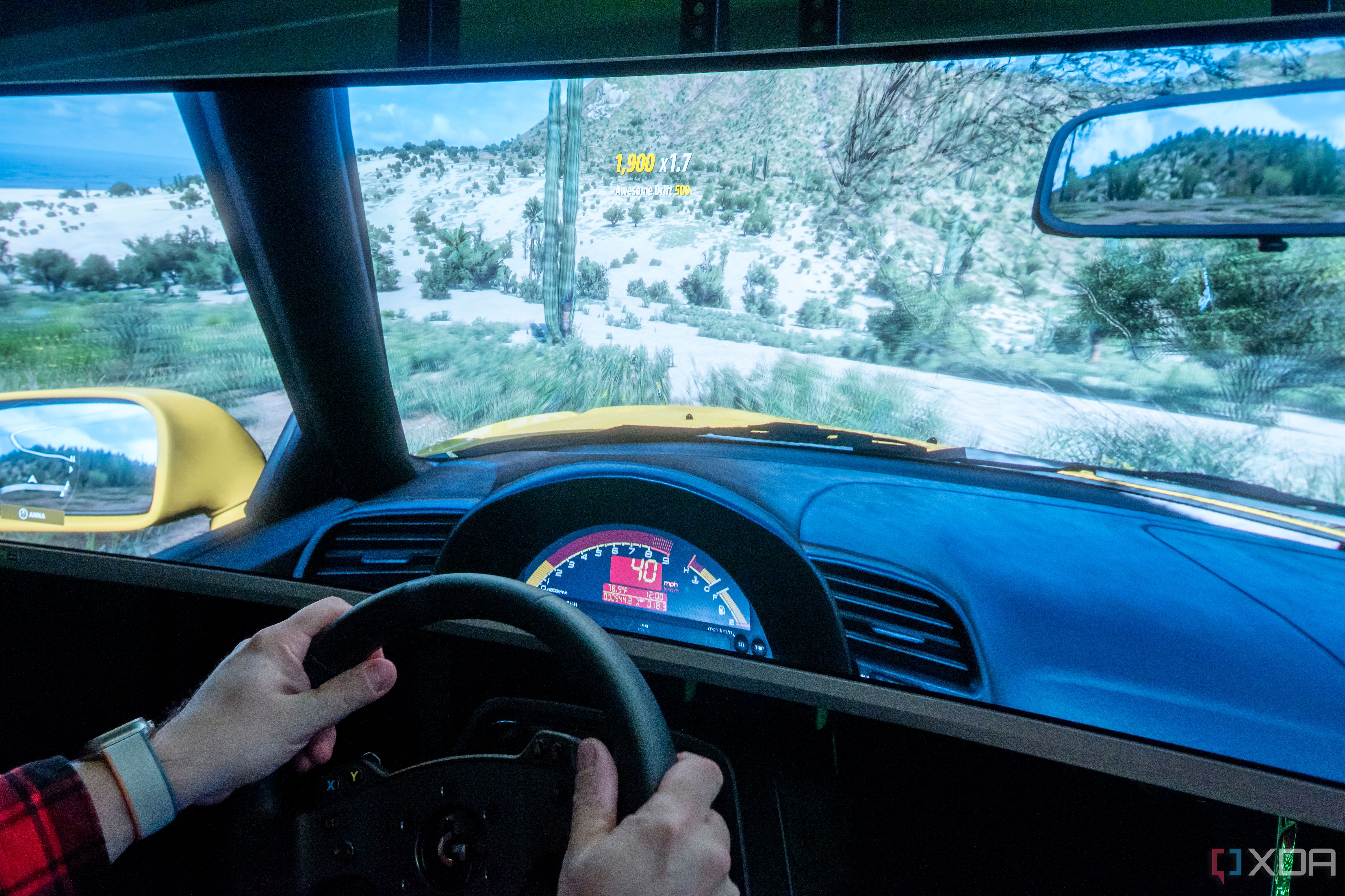 A man sitting in a gaming chair and using a steering wheel to play a videogame on a large monitor