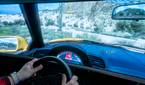A man sitting in a gaming chair and using a steering wheel to play a videogame on a large monitor