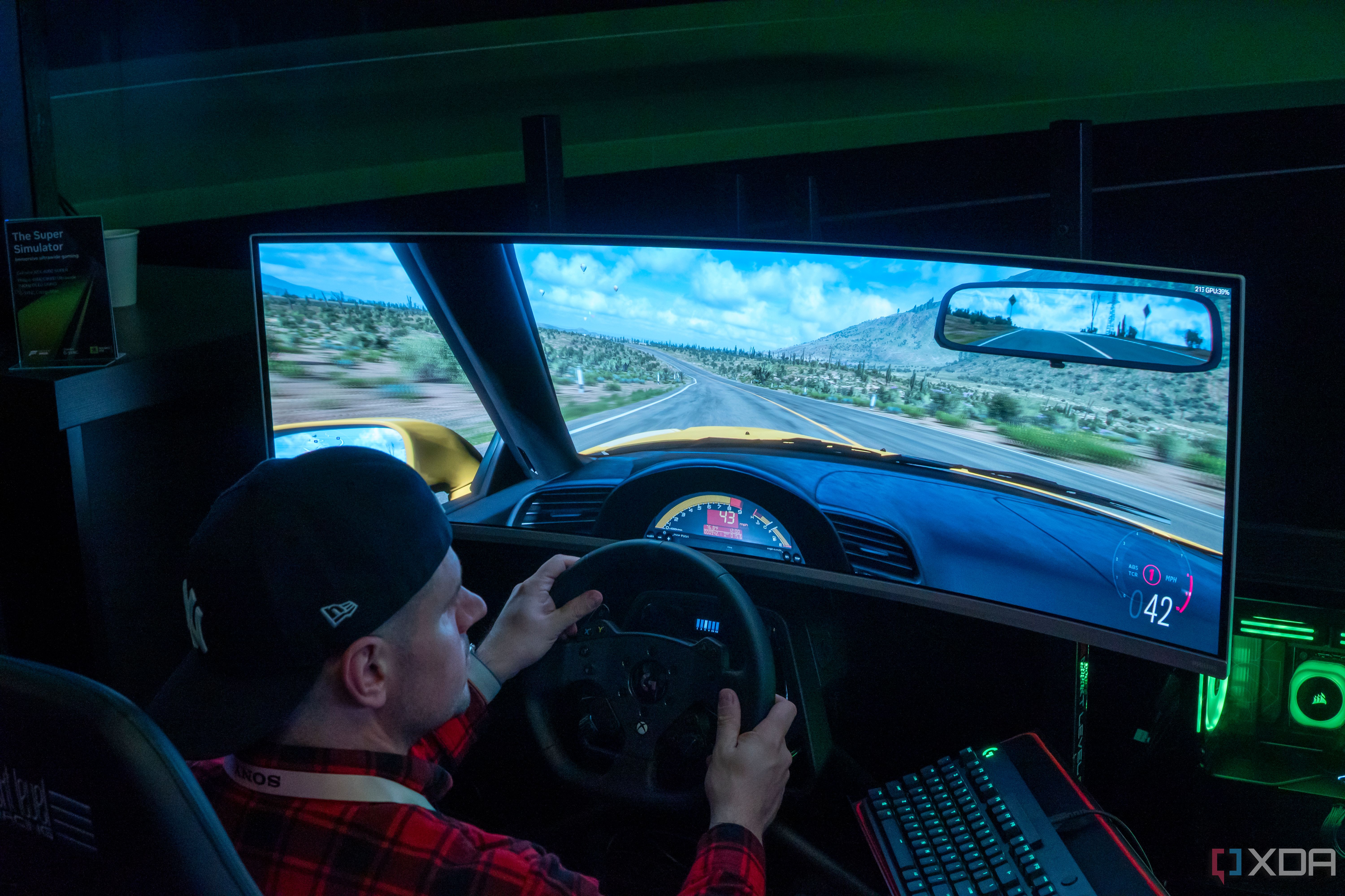 A man sitting in a gaming chair and using a steering wheel to play a videogame on a large monitor