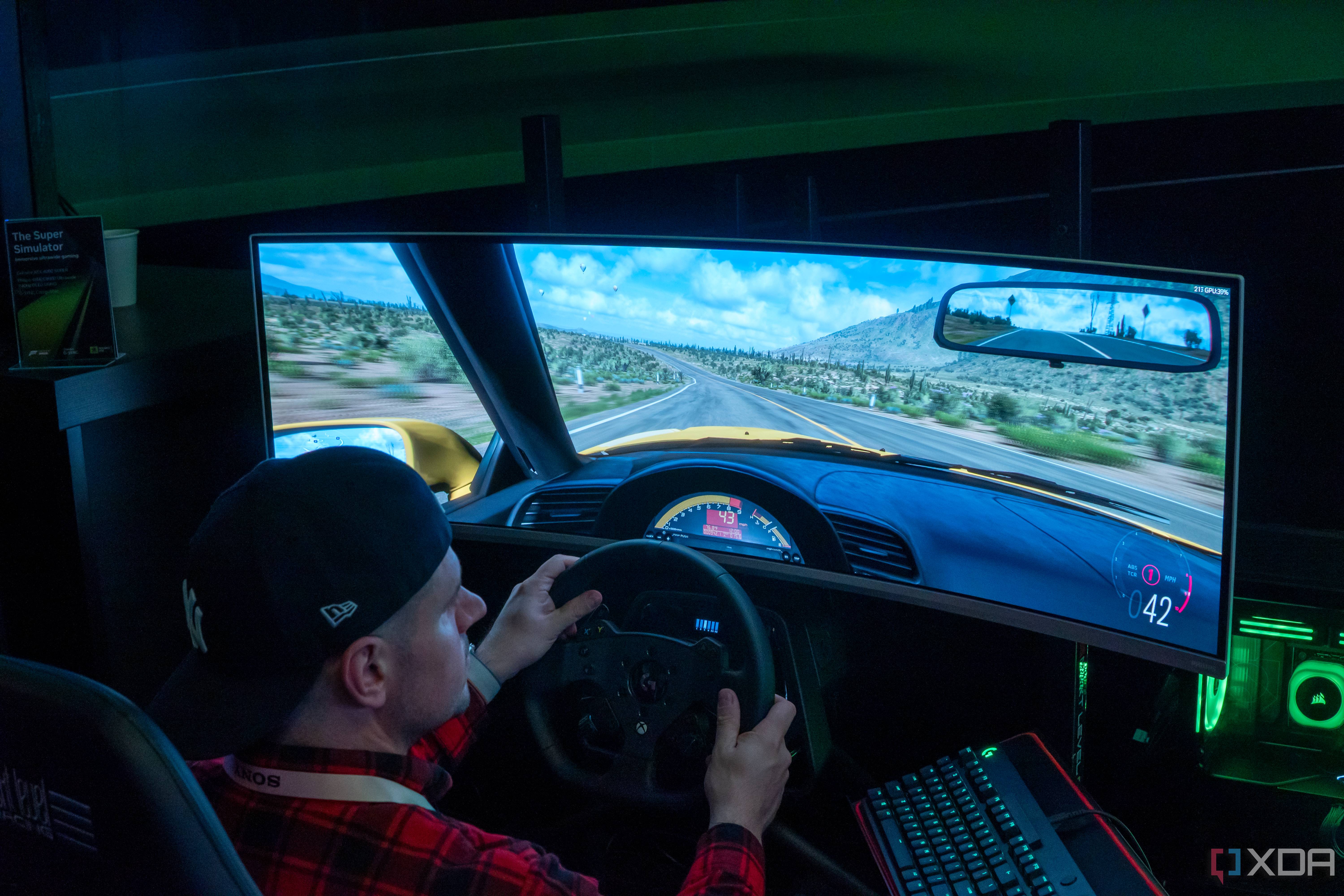 A man sitting in a gaming chair and using a steering wheel to play a videogame on a large monitor