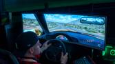 A man sitting in a gaming chair and using a steering wheel to play a videogame on a large monitor