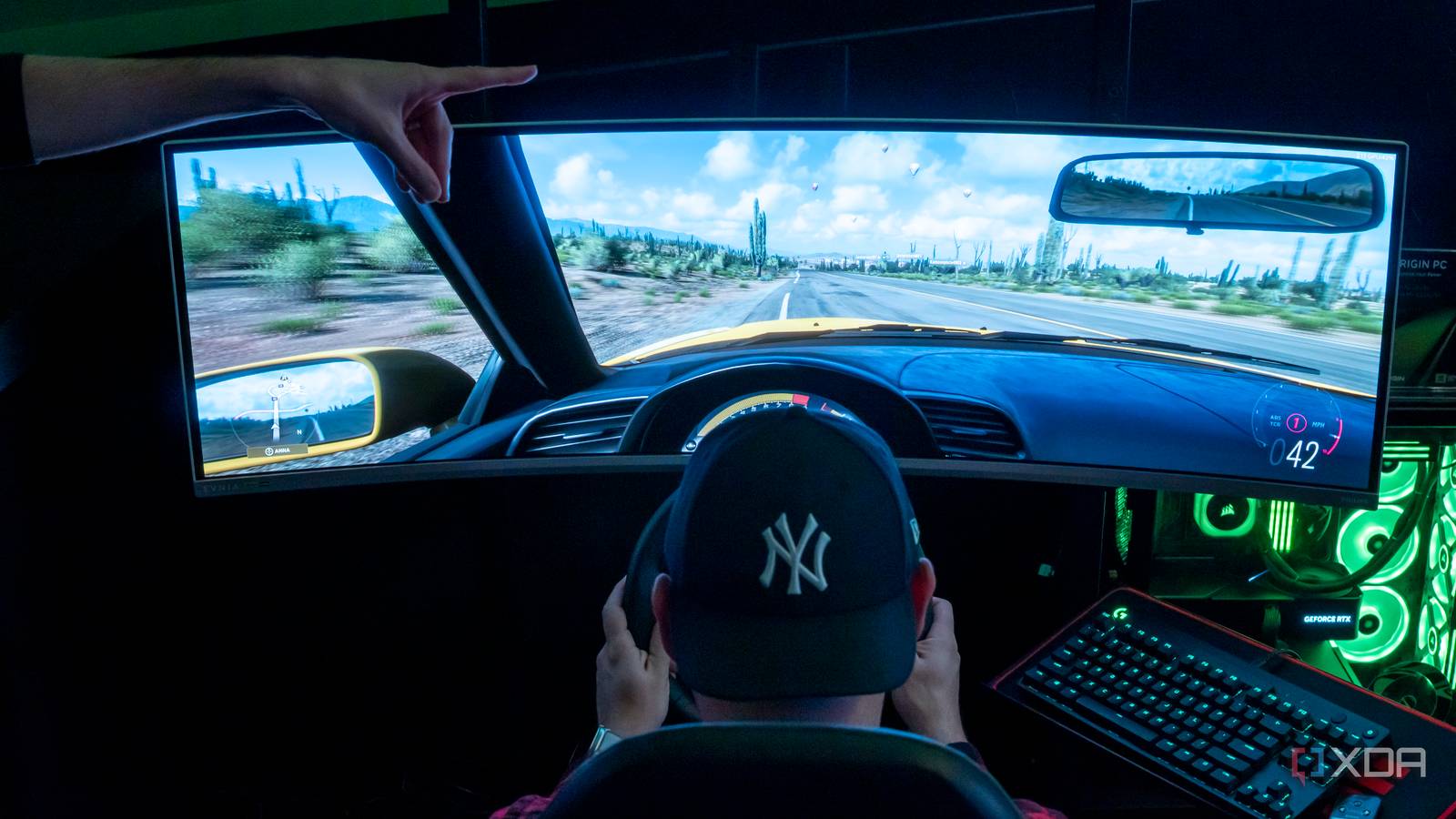 A man sitting in a gaming chair and using a steering wheel to play a videogame on a large monitor