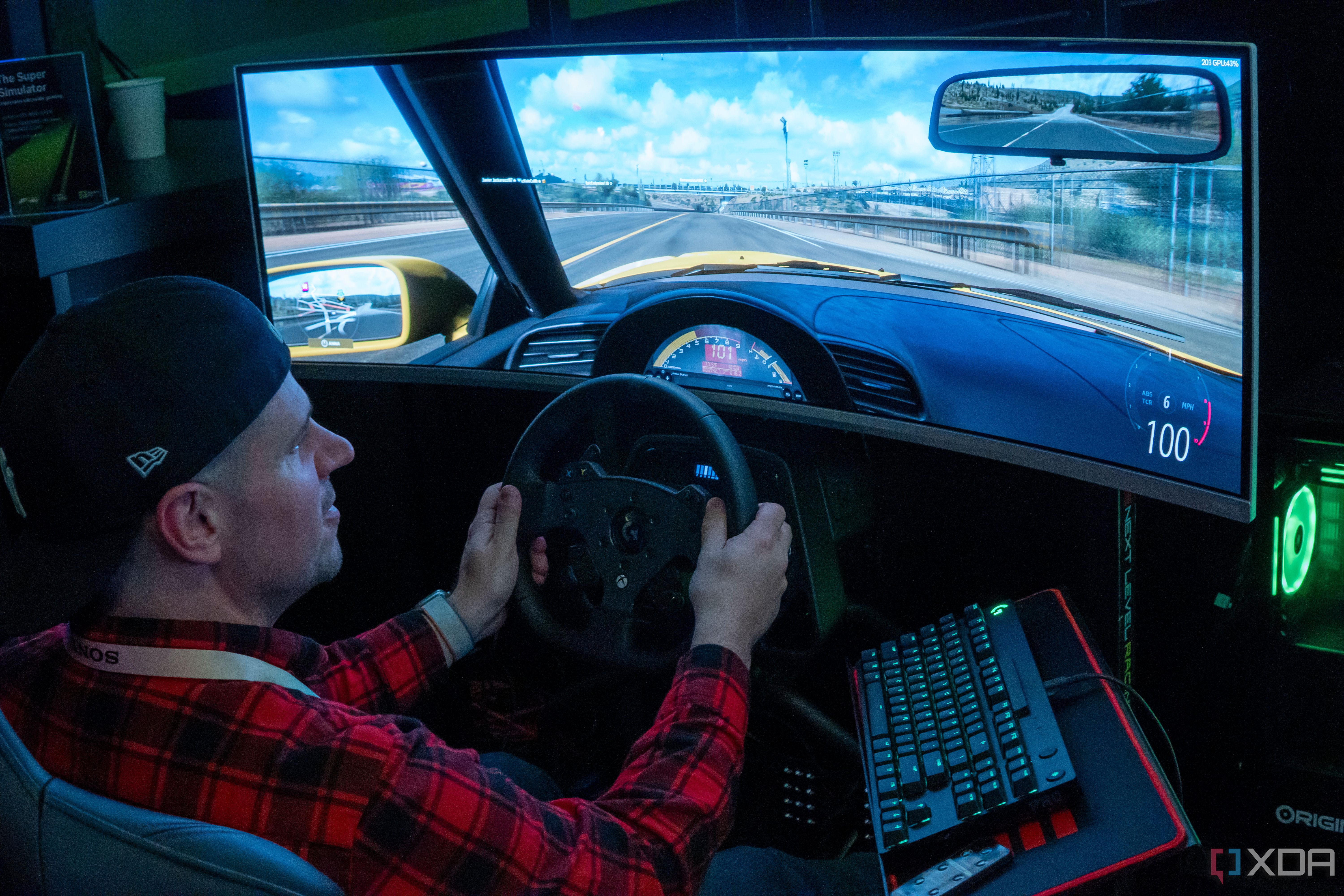 A man sitting in a gaming chair and using a steering wheel to play a videogame on a large monitor