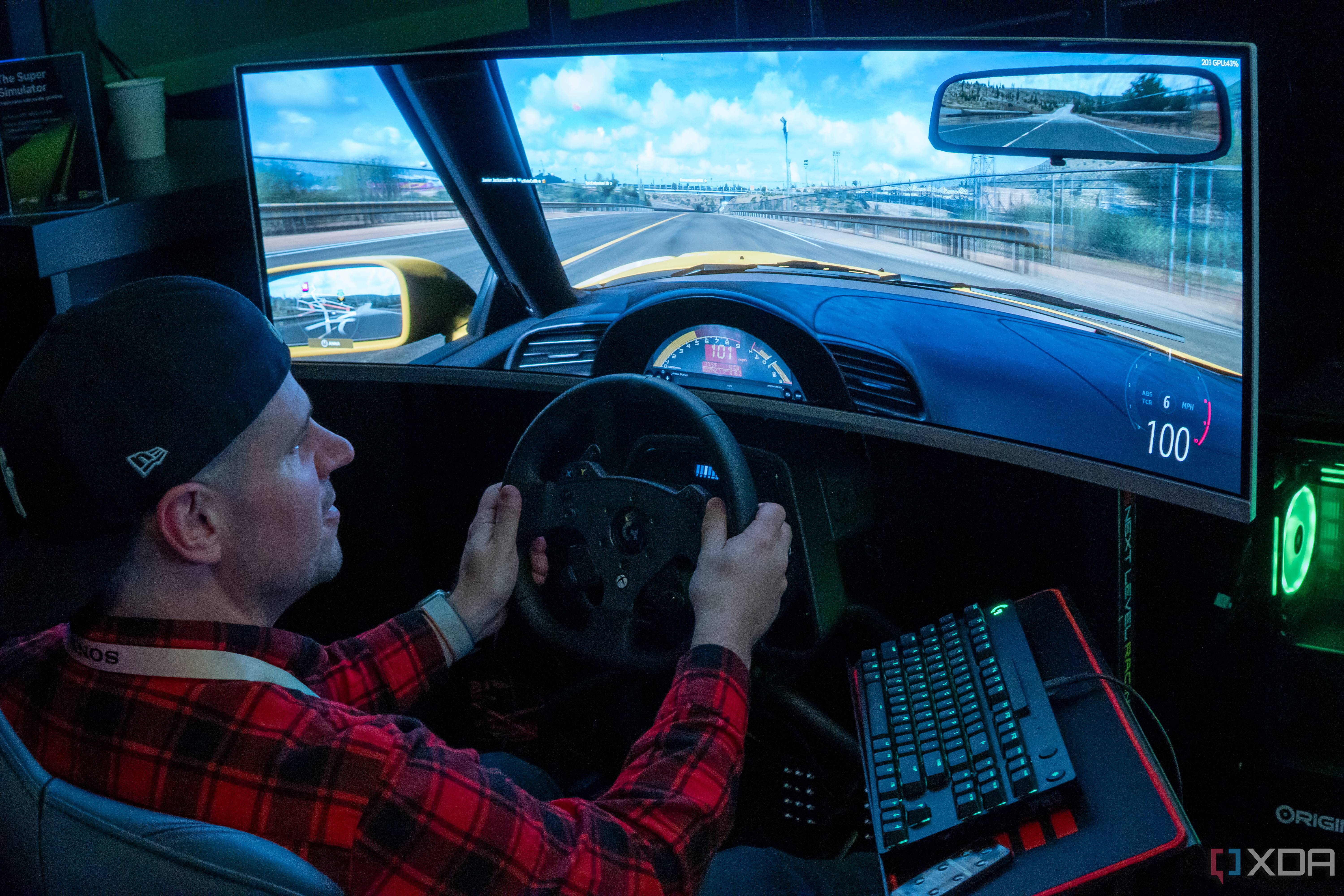 A man sitting in a gaming chair and using a steering wheel to play a videogame on a large monitor