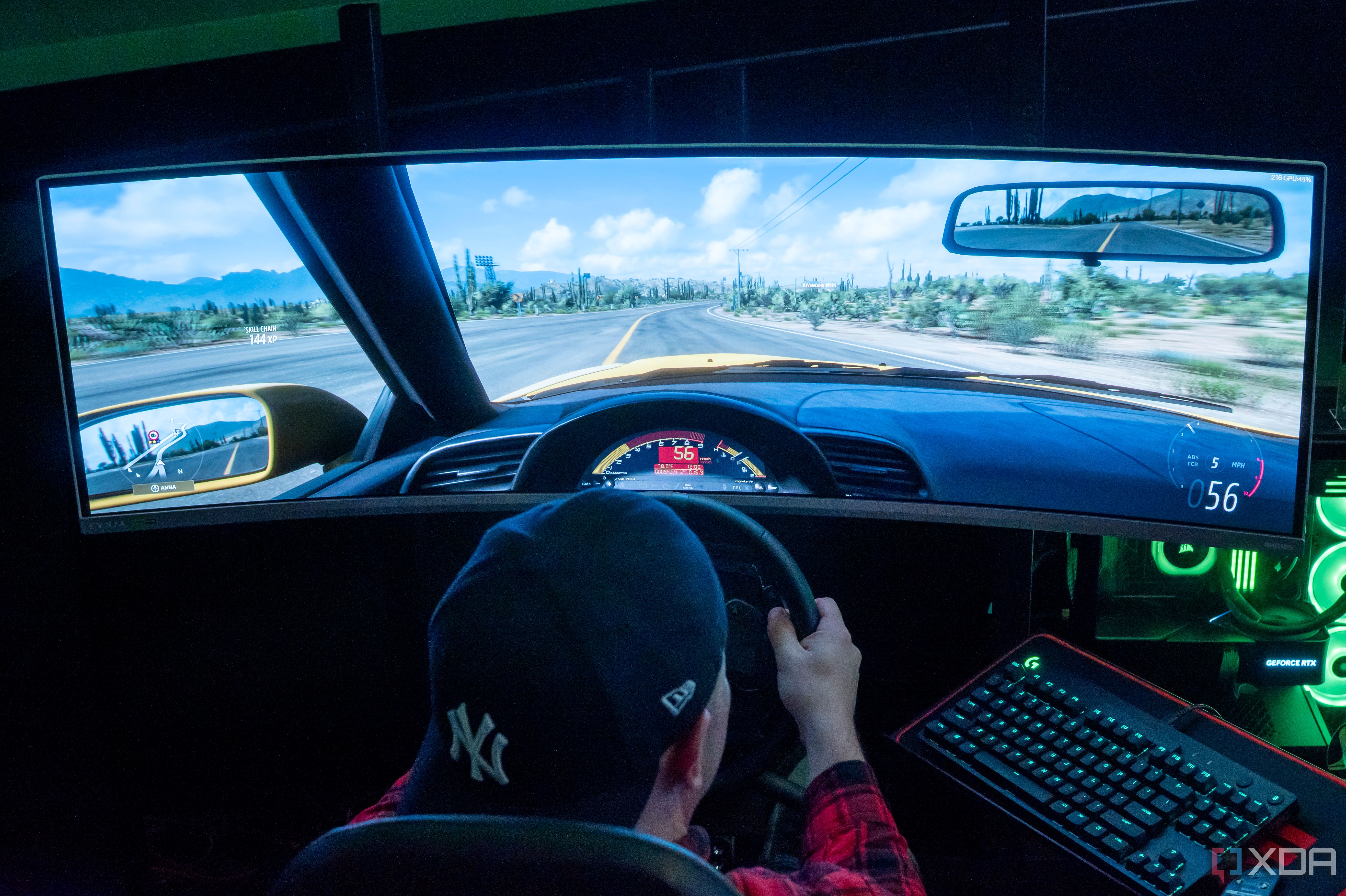 A man sitting in a gaming chair and using a steering wheel to play a videogame on a large monitor