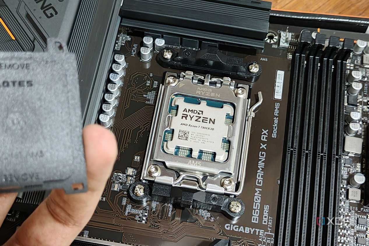 An image showing an AMD Ryzen 7 7800X3D CPU installed on a motherboard with a person in the foreground holding the socket cap in their hand.