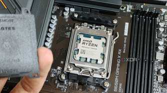 An image showing an AMD Ryzen 7 7800X3D CPU installed on a motherboard with a person in the foreground holding the socket cap in their hand.