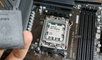 An image showing an AMD Ryzen 7 7800X3D CPU installed on a motherboard with a person in the foreground holding the socket cap in their hand.